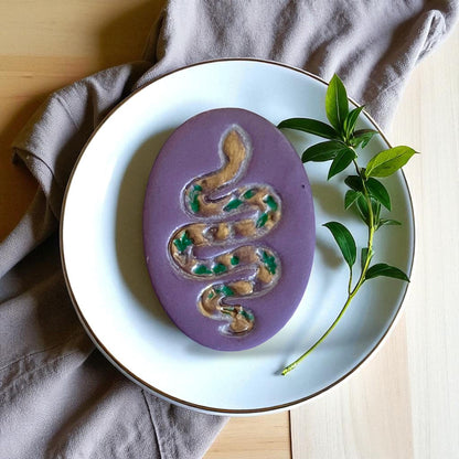 Purple clay piece with painted snake design and leaves