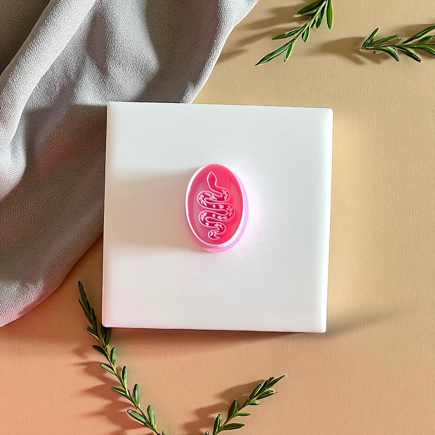 Pink snake clay cutter on white tile with leaves