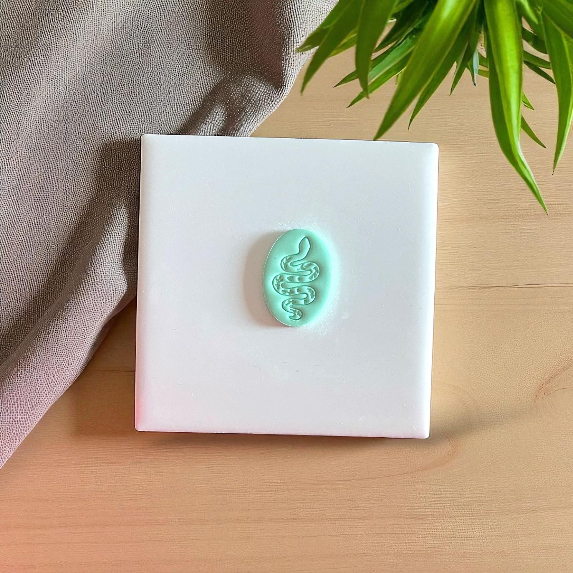 Small teal snake clay design on white tile
