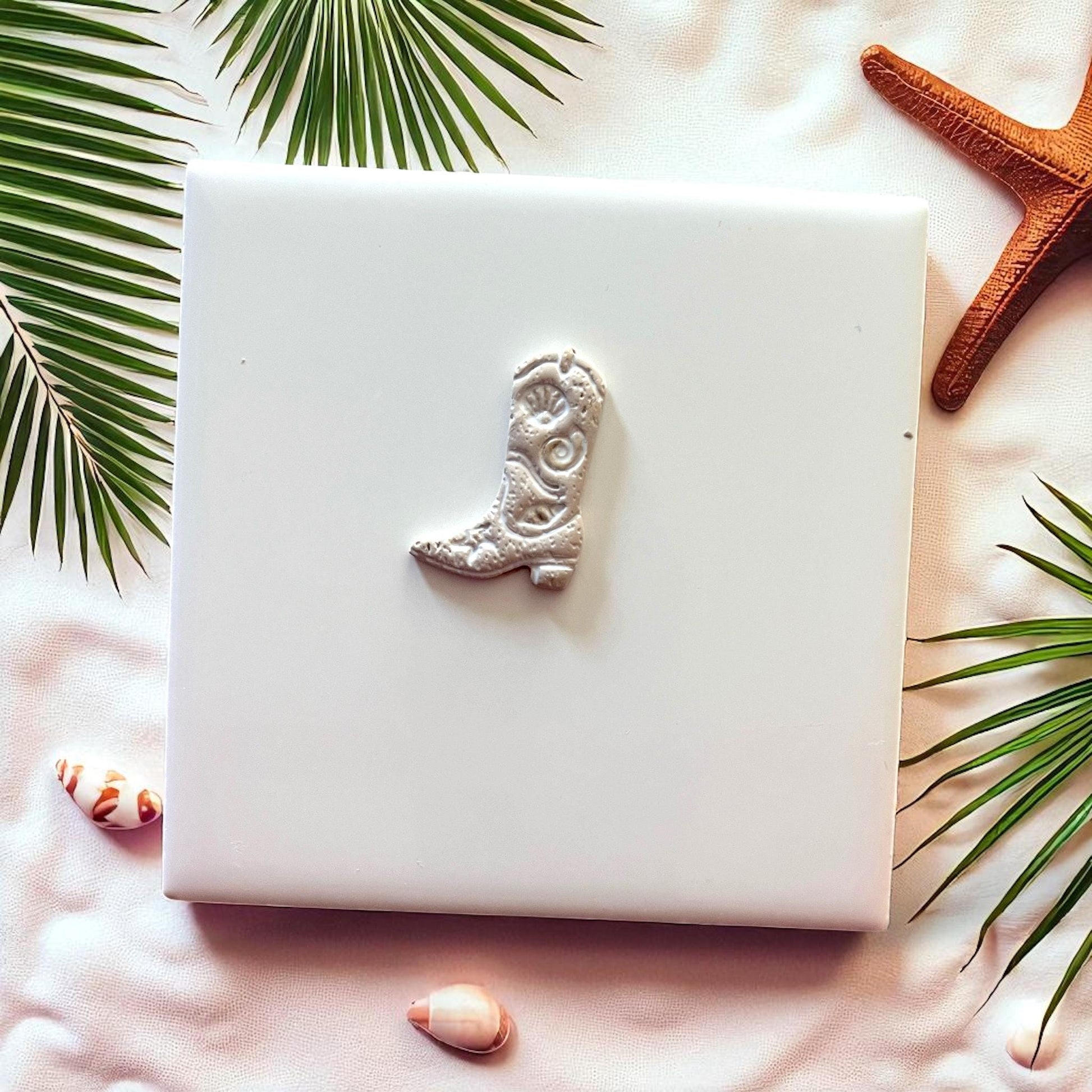 Small coastal cowboy boot clay design on white tile with seashells