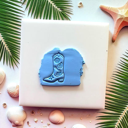 Blue cowboy boot clay impression on white tile with seashells