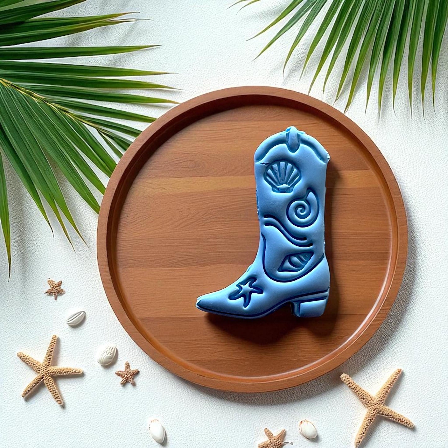 Blue coastal cowboy boot clay design on wood plate with palm leaves
