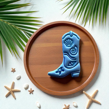 Blue coastal cowboy boot clay design on wood plate with palm leaves