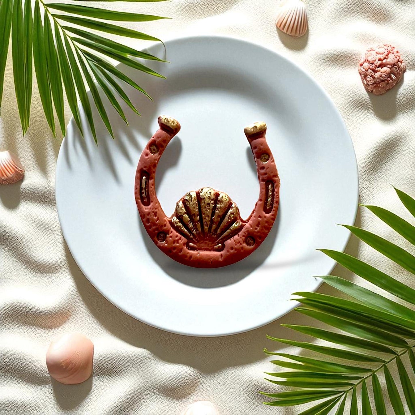 Clay horseshoe with seashell design on white plate with palm leaves