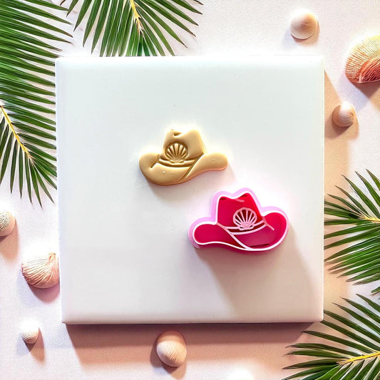 Clay cowboy hat with seashell next to pink cutter on white tile