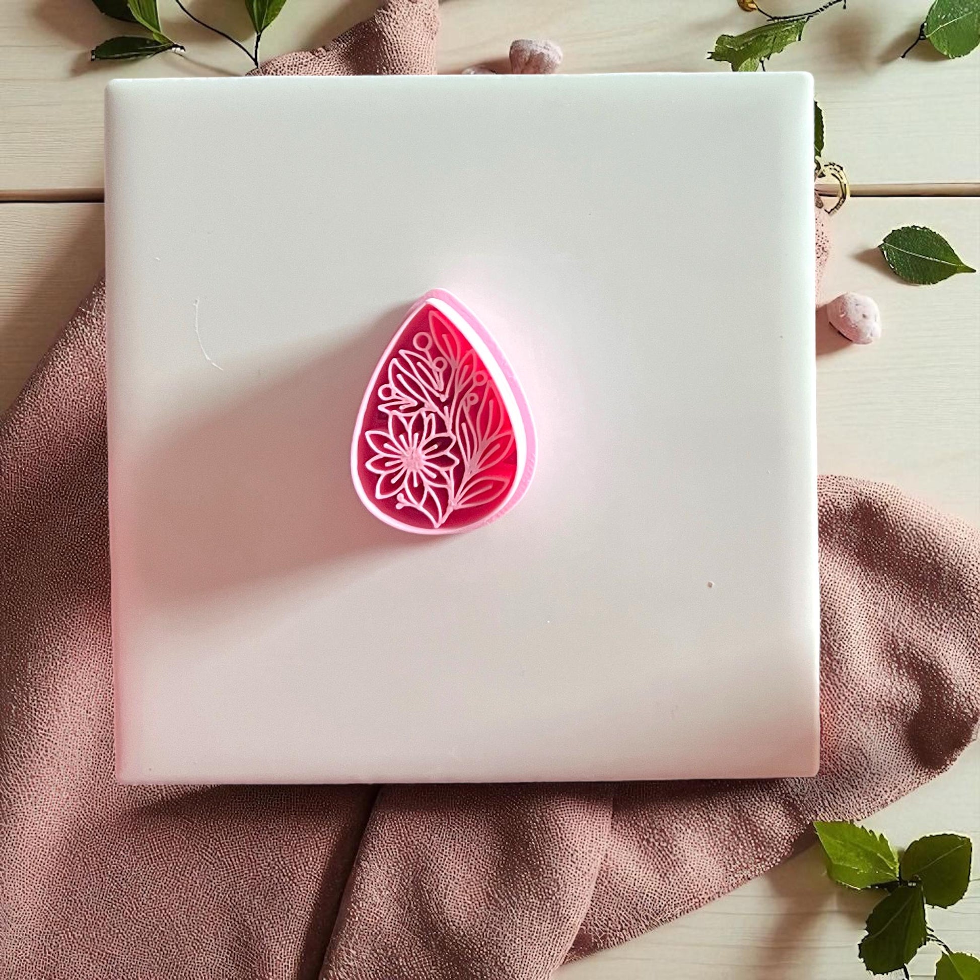 Pink floral teardrop cutter displayed on white tile with fabric and greenery.