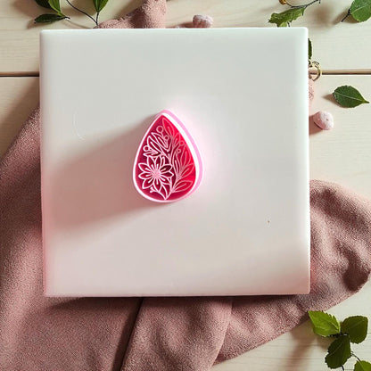 Pink floral teardrop cutter displayed on white tile with fabric and greenery.
