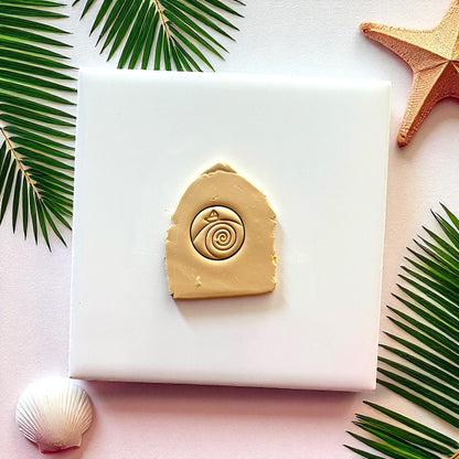 Tan clay imprint of paper boat in waves design on white tile with palm leaves and starfish.
