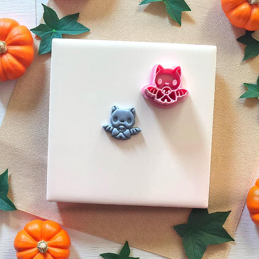 Gray baby bat clay piece beside pink bat cutter on white tile with pumpkins.