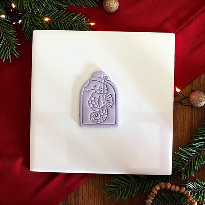Purple seahorse clay imprint on white tile with red fabric and Christmas decorations.