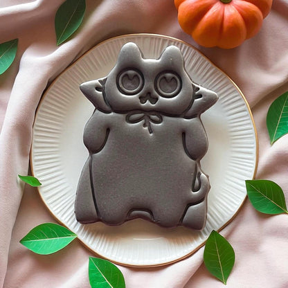 Large grey cat clay imprint with heart eyes on a white plate surrounded by leaves.