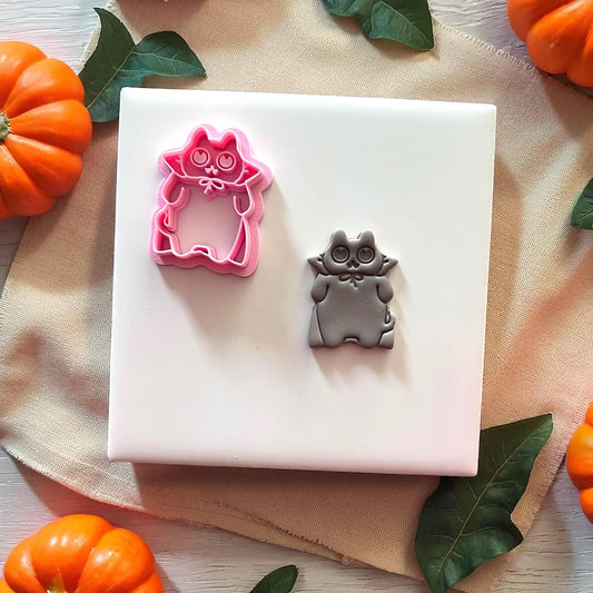 Pink Halloween cat clay cutter with grey imprint on white tile and pumpkins.