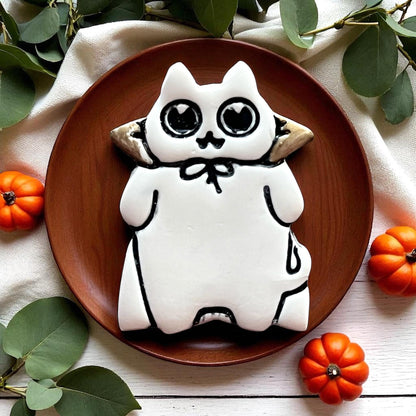 White decorated Halloween cat cookie with heart eyes on a brown plate with pumpkins.