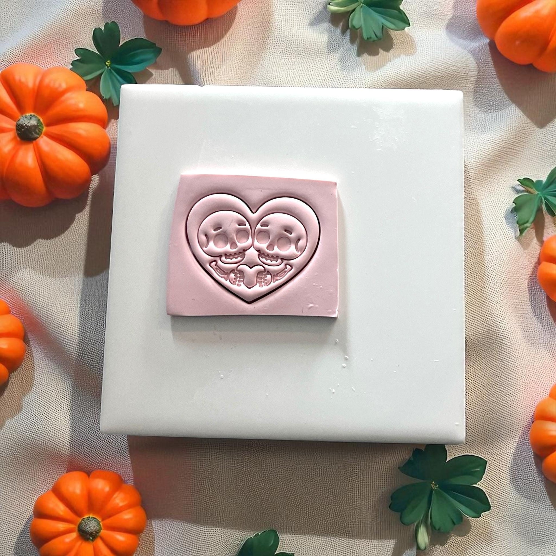 Pink clay skeleton couple heart design on white tile with pumpkins