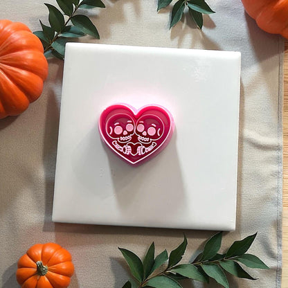 Pink skeleton couple heart cutter on tile surrounded by greenery