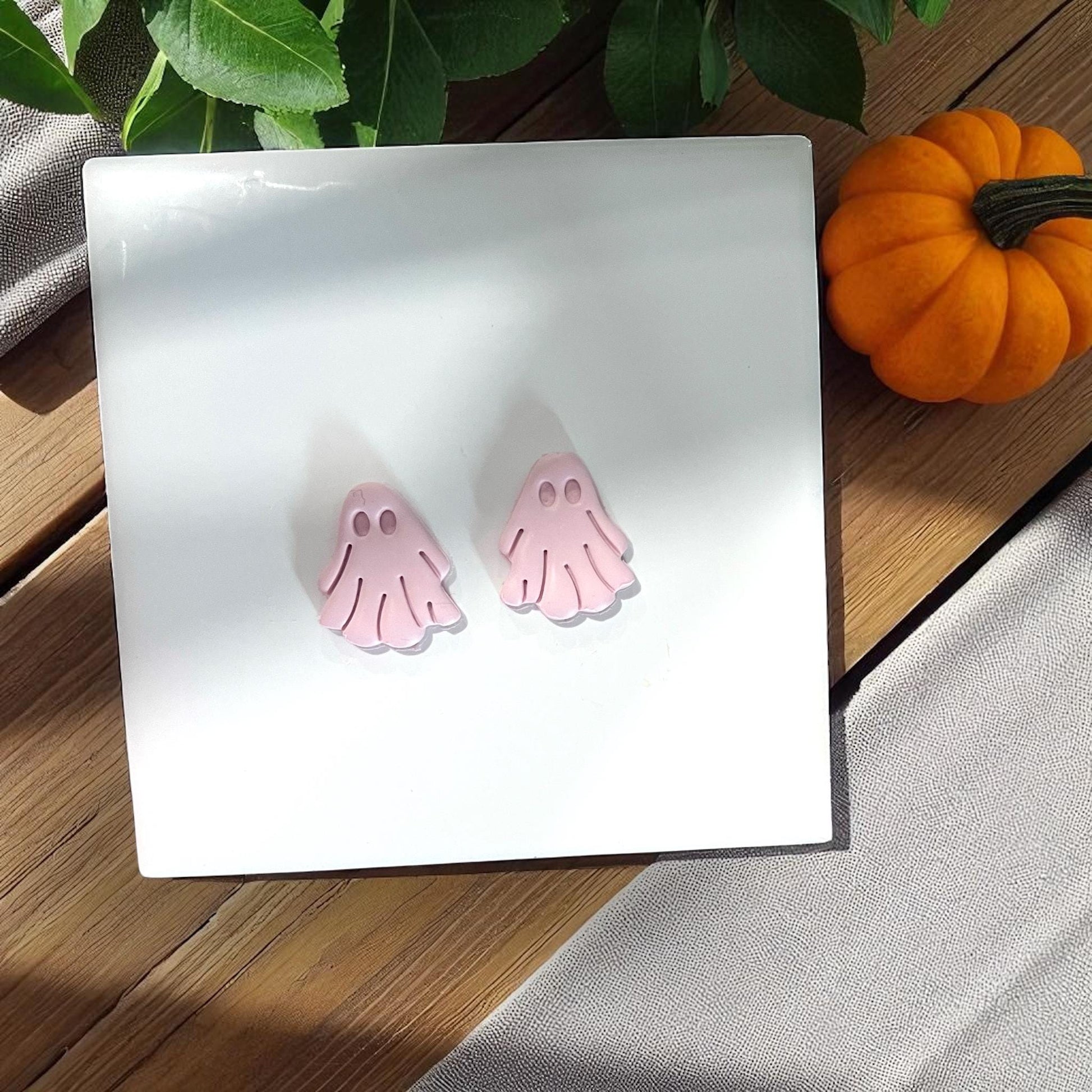Two small pink clay ghosts on white tile with pumpkin