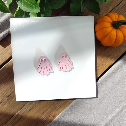 Two small pink clay ghosts on white tile with pumpkin
