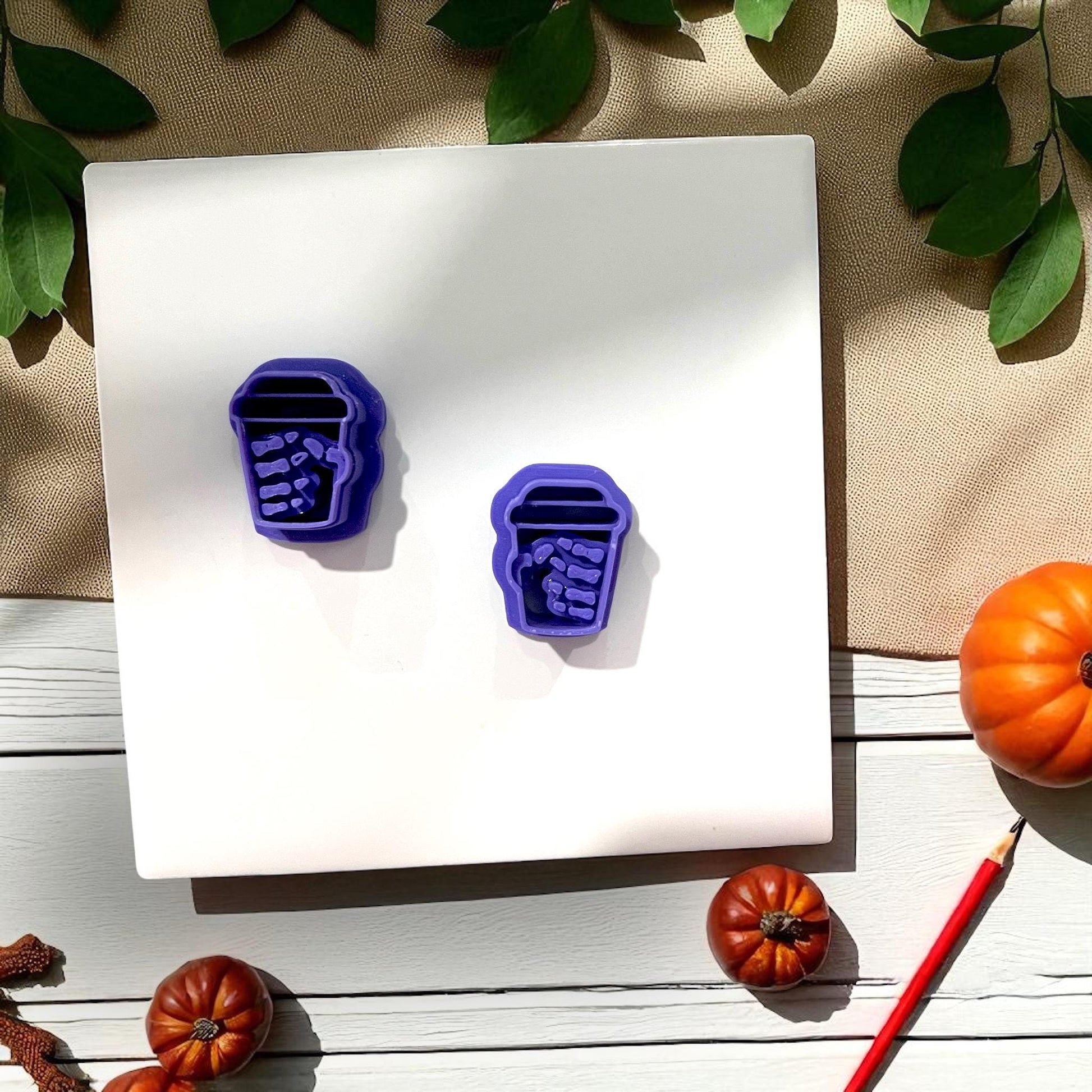 Purple skeleton hand coffee cup cutters on white tile with pumpkin