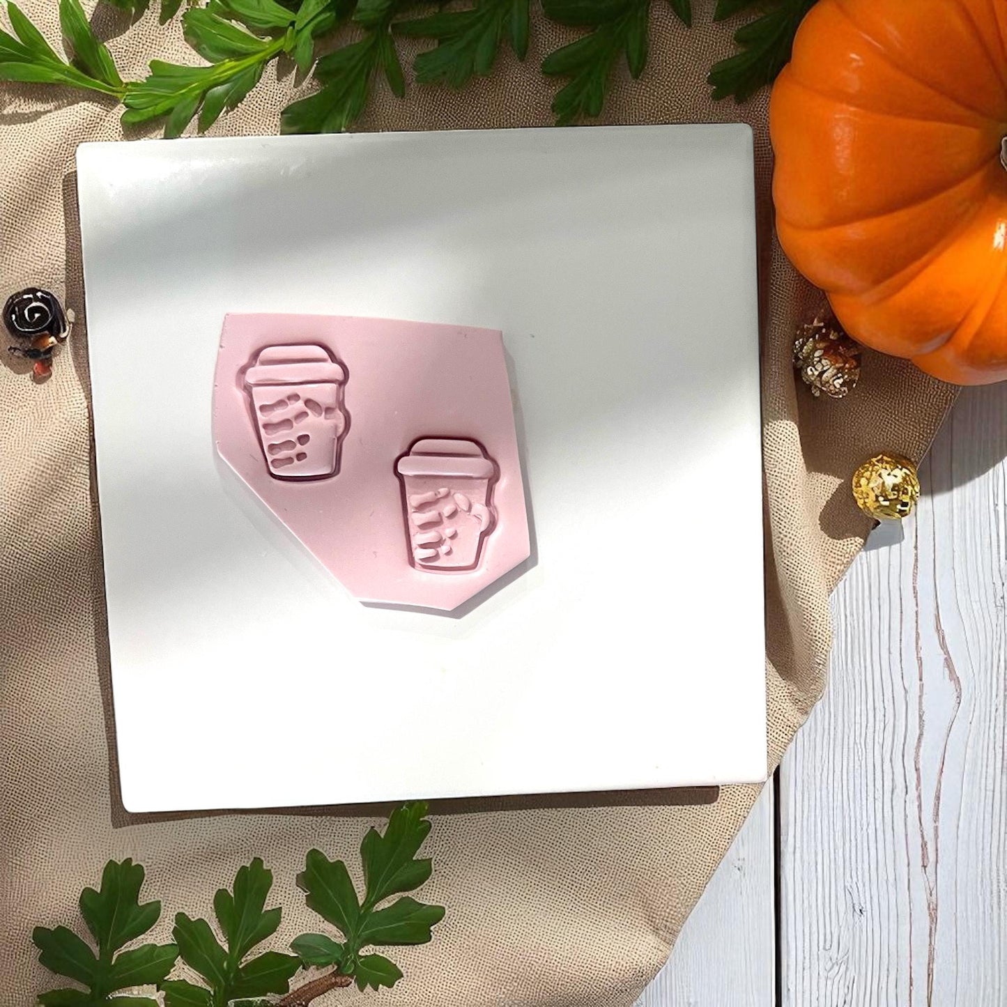 Pink clay slab with skeleton coffee cup impressions and pumpkin nearby