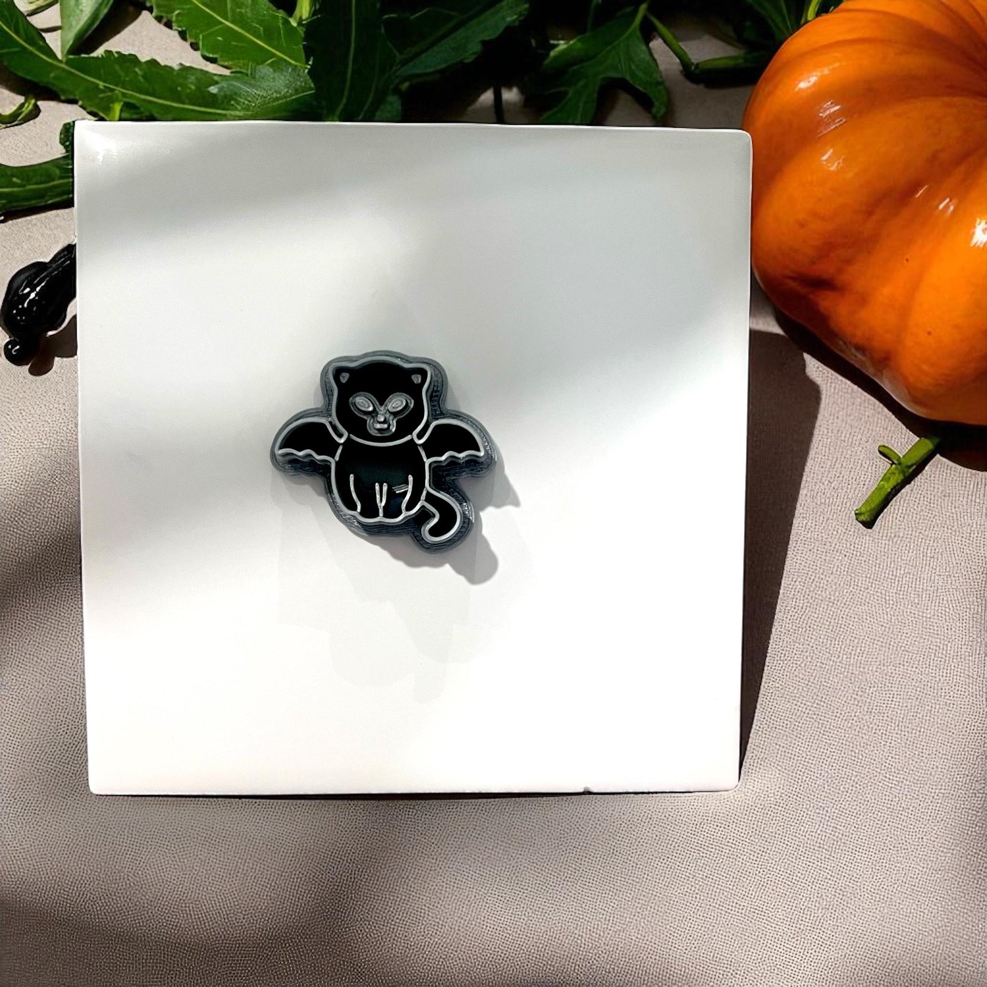 Black vampire kitten cutter on white tile with pumpkin