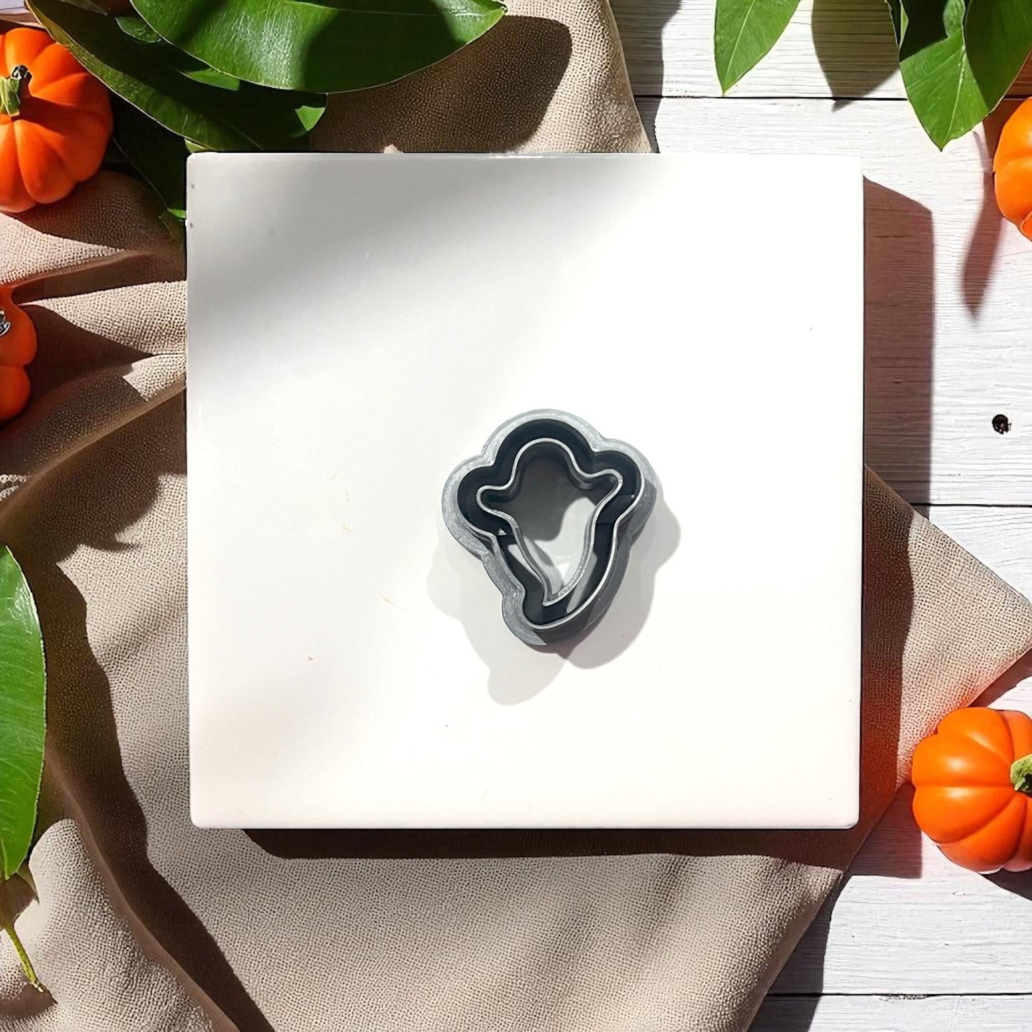 Thin ghost silhouette clay cutter on white tile with pumpkins