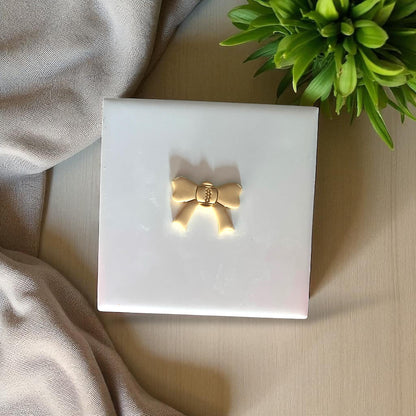 Small gold football bow clay piece on white tile
