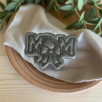 Gray football mom clay piece with bow on fabric in wooden bowl