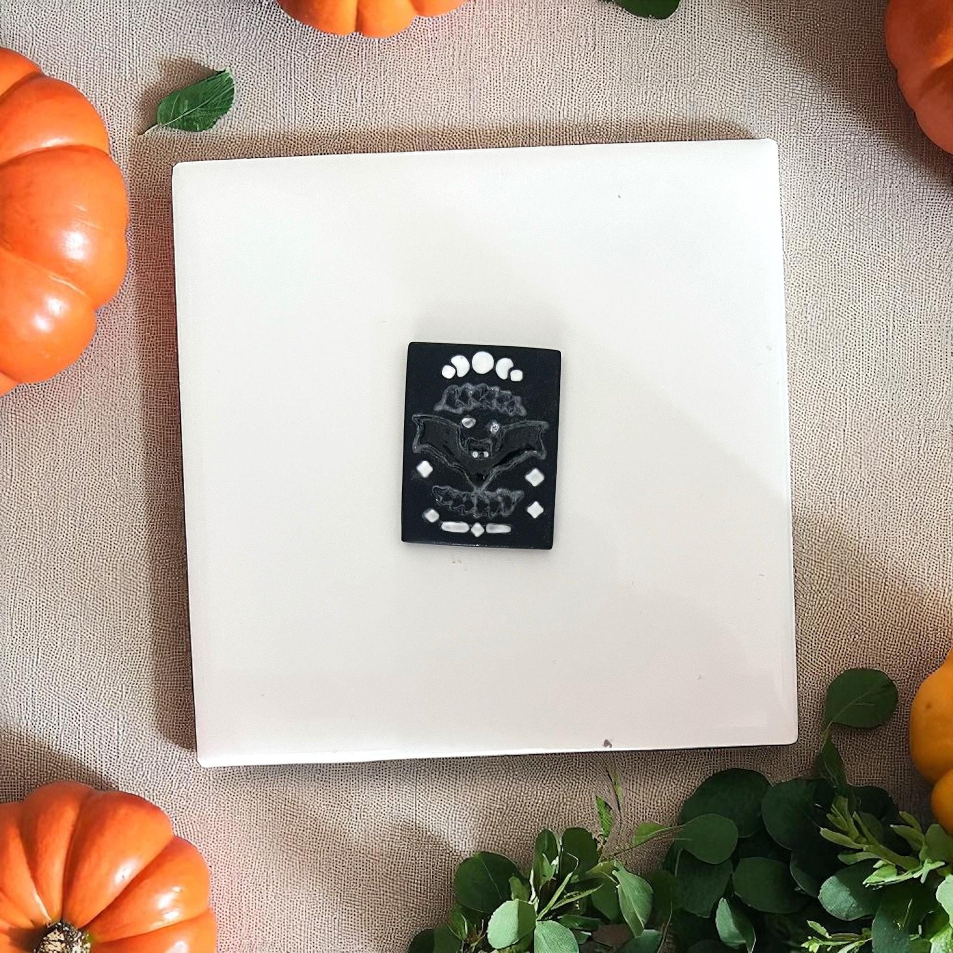 Black clay rectangle imprint of bat with moon phases on white tile.