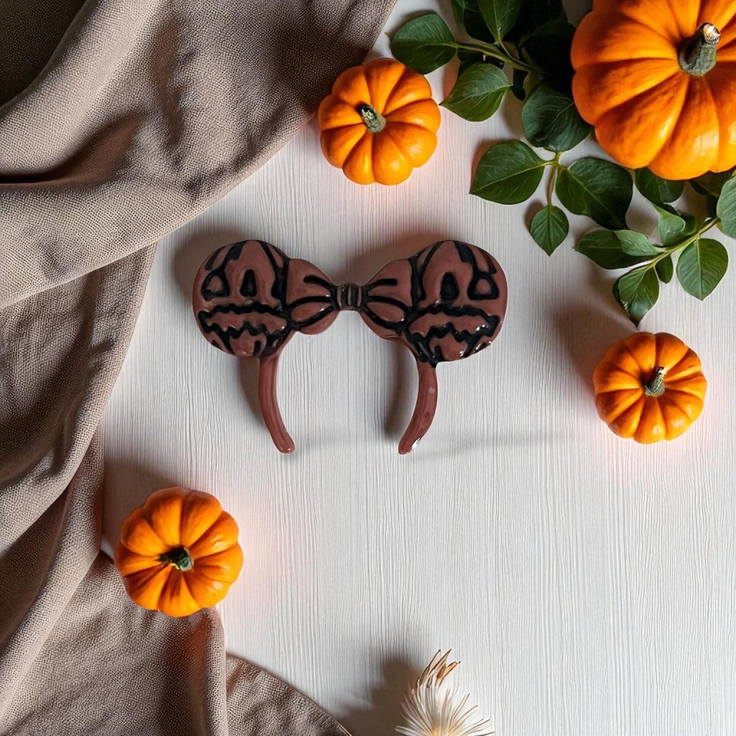 Pumpkin bow ears clay imprint on white surface with pumpkins and greenery.