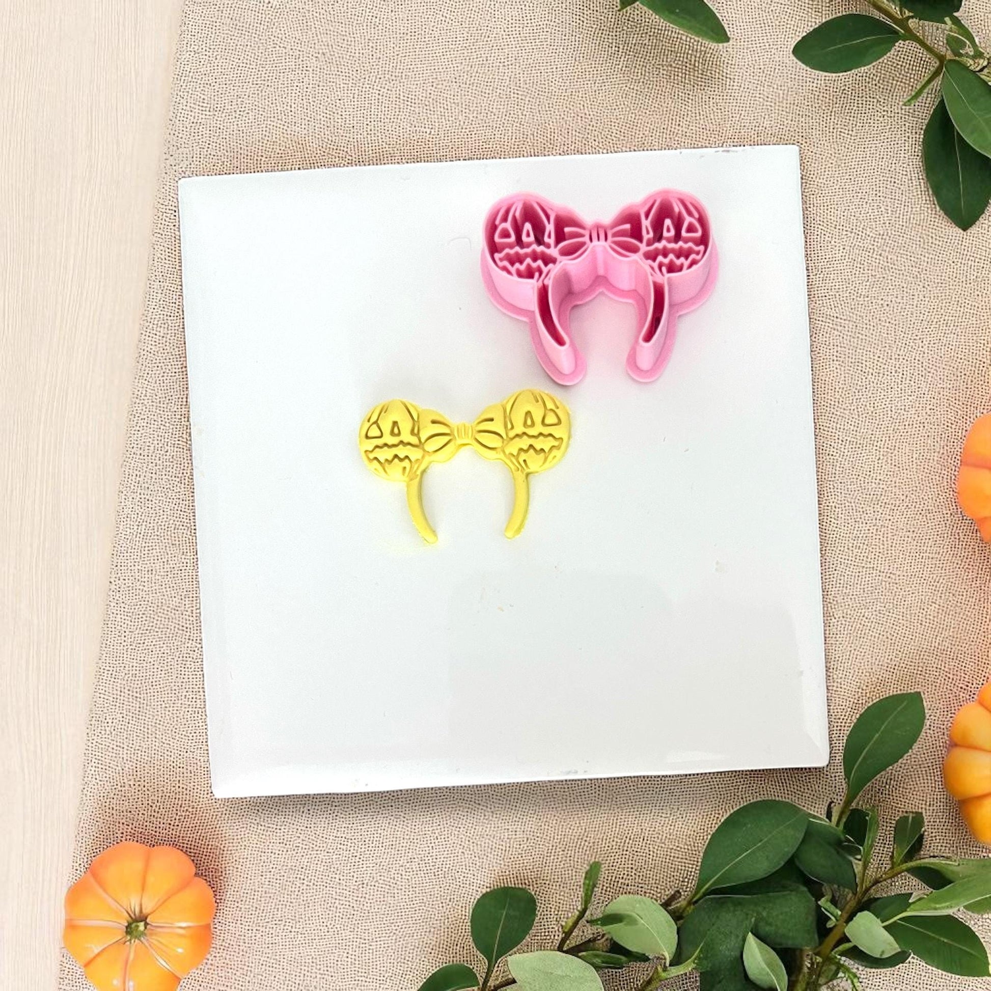 Pink pumpkin ears cutter with yellow clay imprint on white tile.