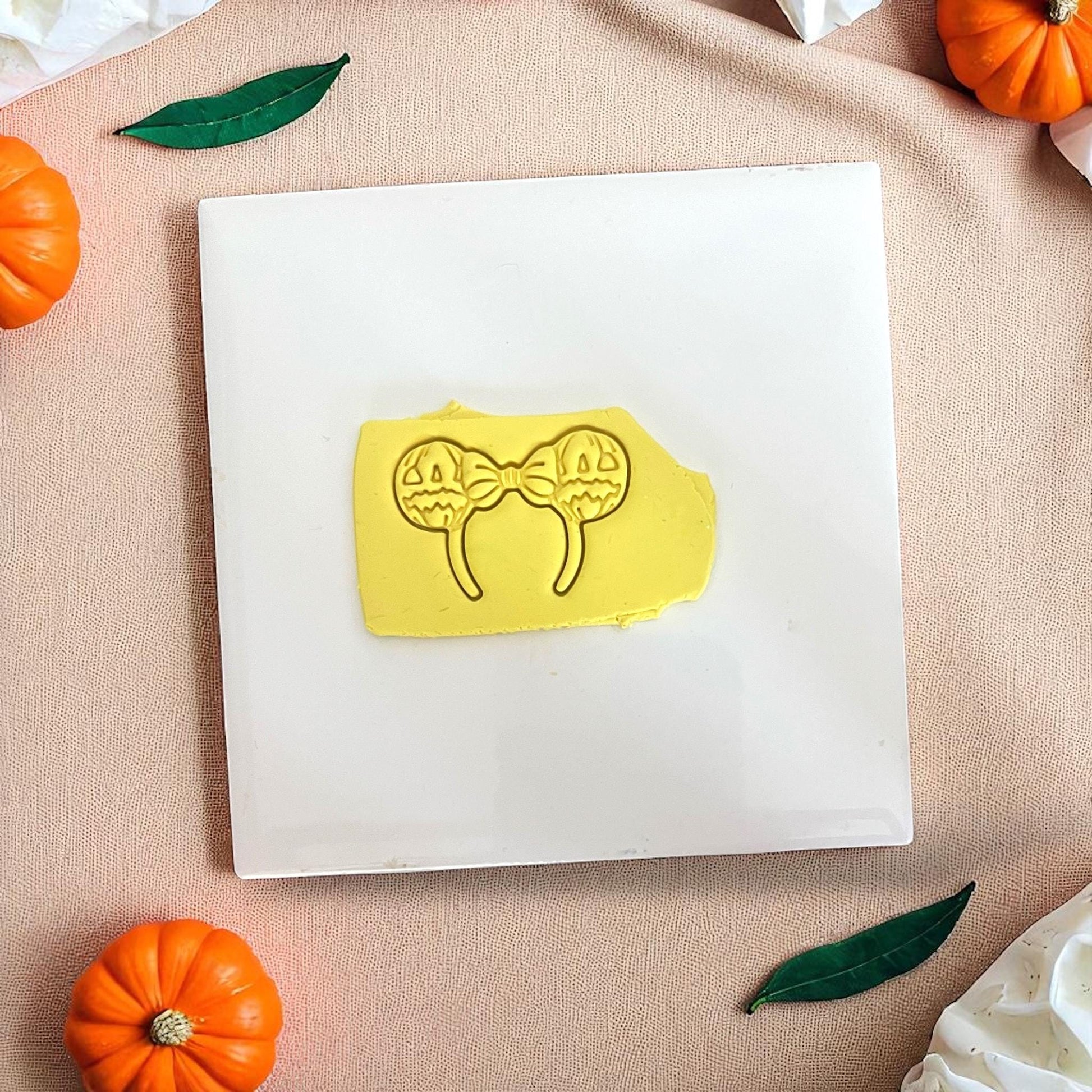 Yellow clay imprint of pumpkin bow ears cutter on white tile with pumpkins.