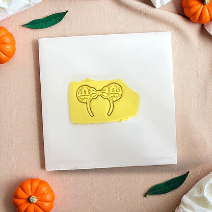 Yellow clay imprint of pumpkin bow ears cutter on white tile with pumpkins.