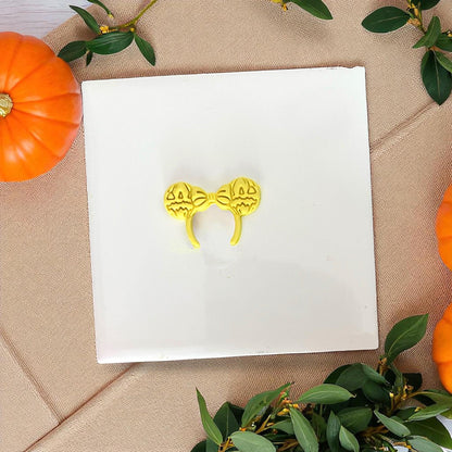 Yellow pumpkin bow ears clay imprint on white tile with greenery and pumpkins.