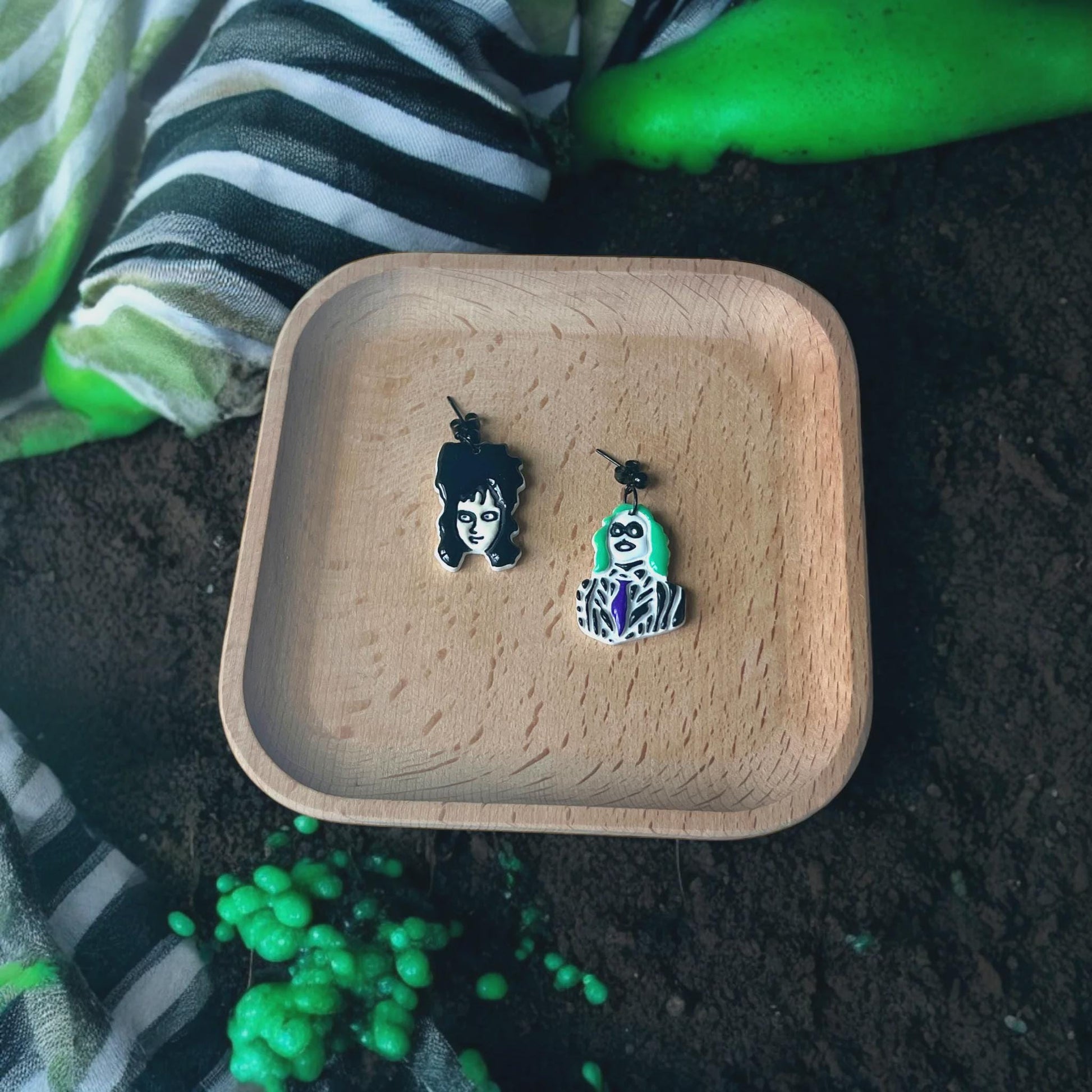 Finished Beetlejuice and Lydia clay earrings on wooden tray with spooky background