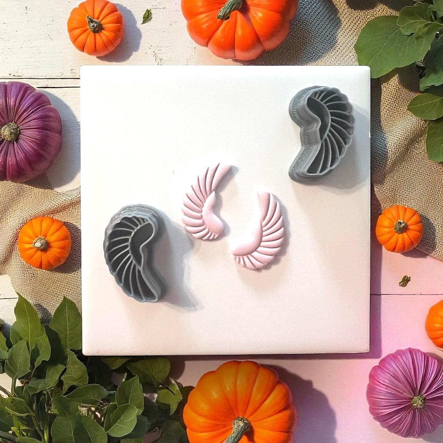 Scarab wing clay cutters with pink clay impressions on white tile and pumpkins