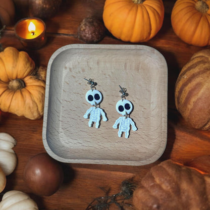 Cute skeleton clay earrings with big eyes on wooden dish and pumpkins