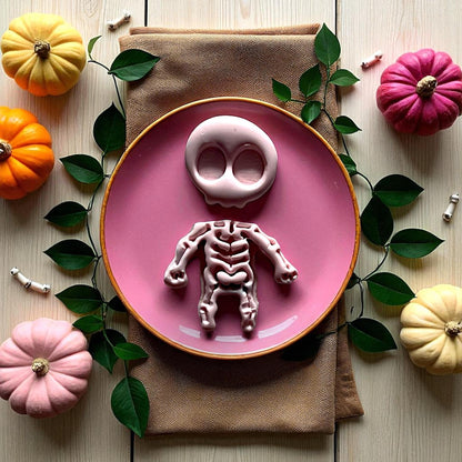 Pink skeleton clay piece on round plate with pumpkins and greenery
