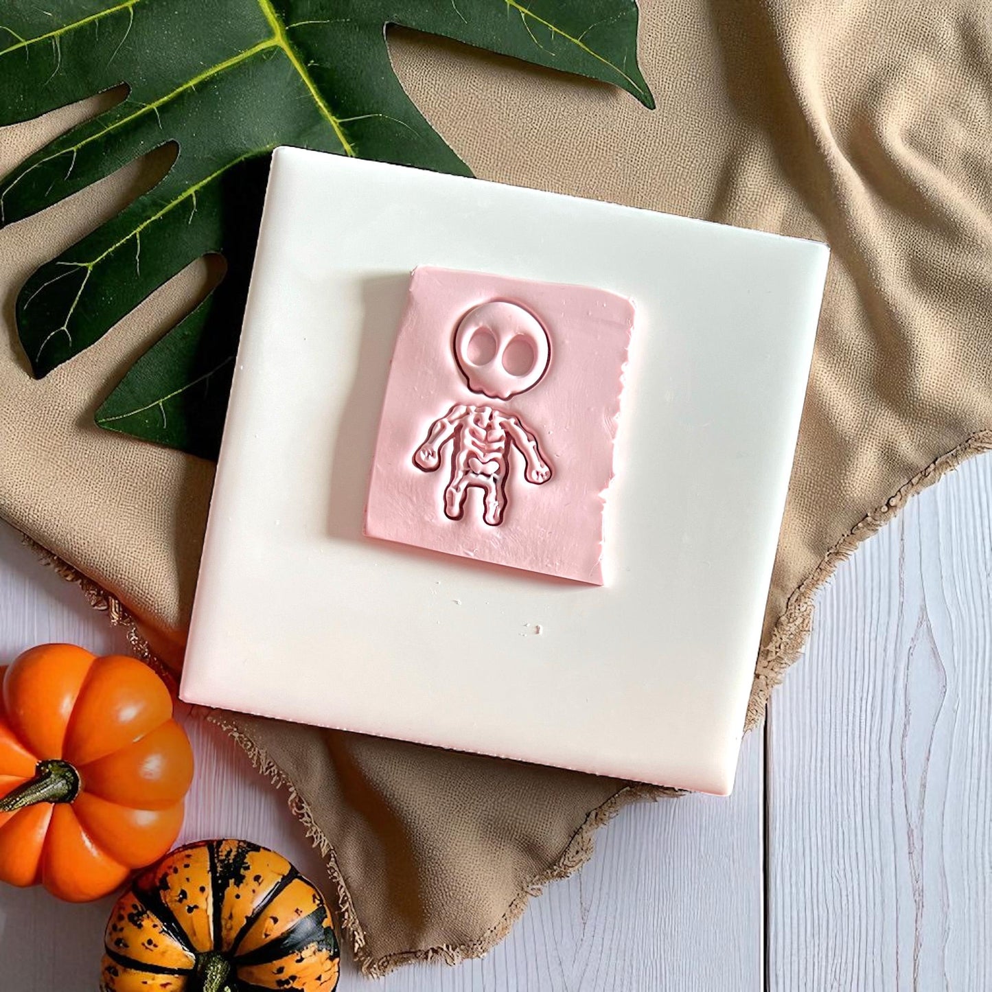 Pink clay slab with skeleton impression on white tile and pumpkins