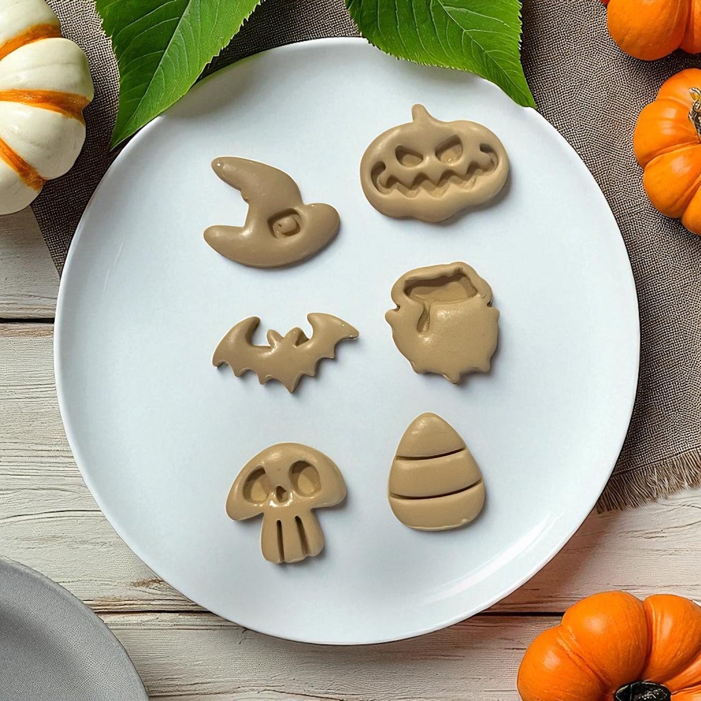 Brown clay Halloween shapes on white plate with leaves and pumpkins