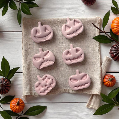 Pink pumpkin face clay shapes on fabric with fall leaves and pumpkins