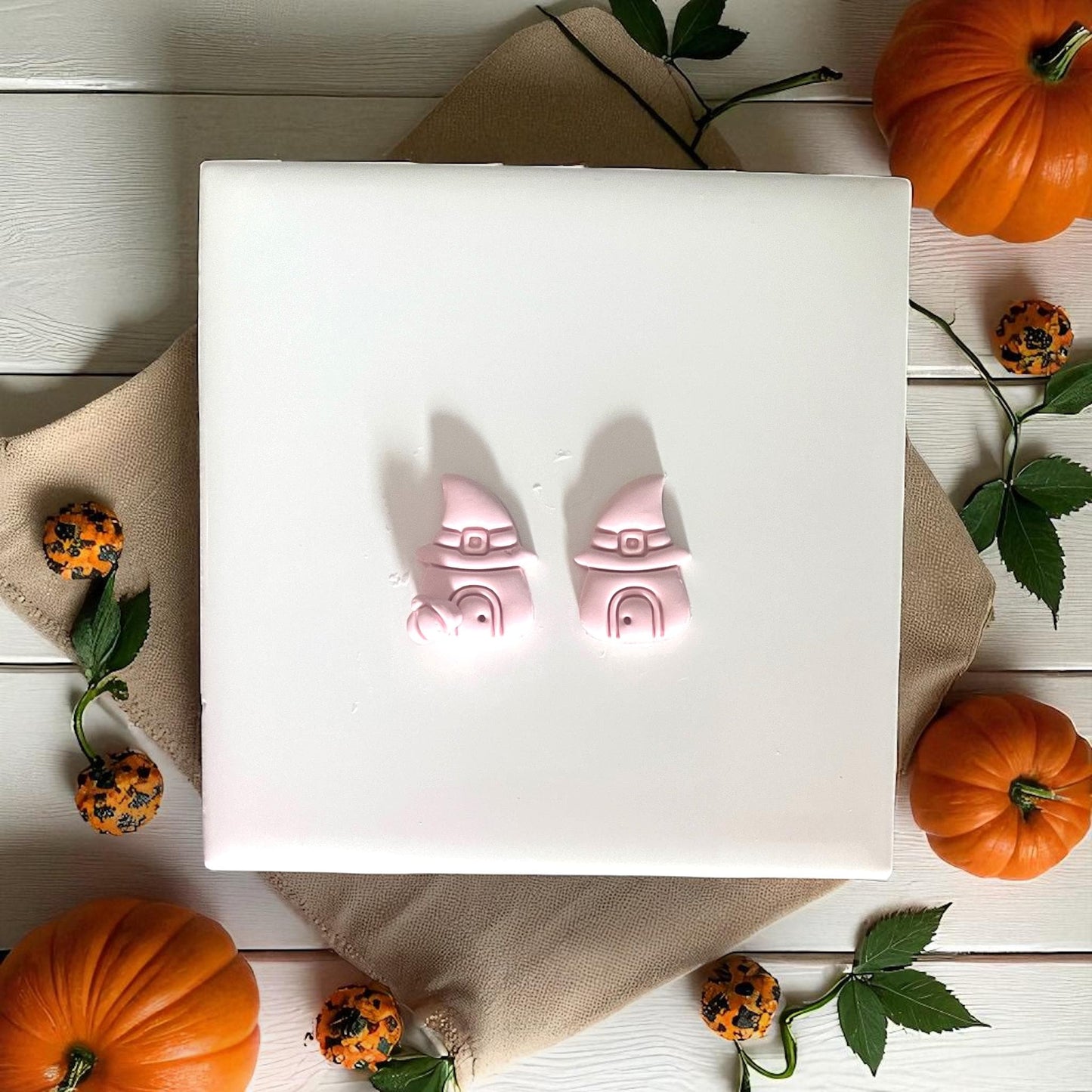 Two pink clay witch hat houses on tile with pumpkins