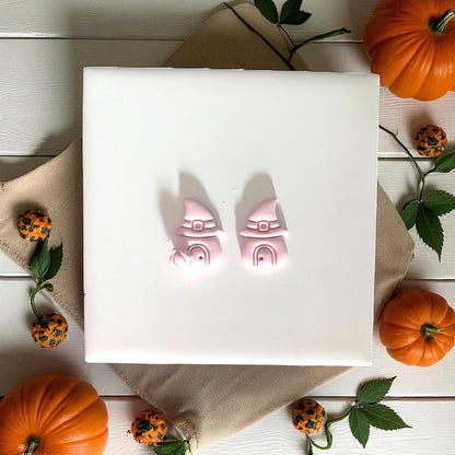 Two pink clay witch hat houses on tile with pumpkins