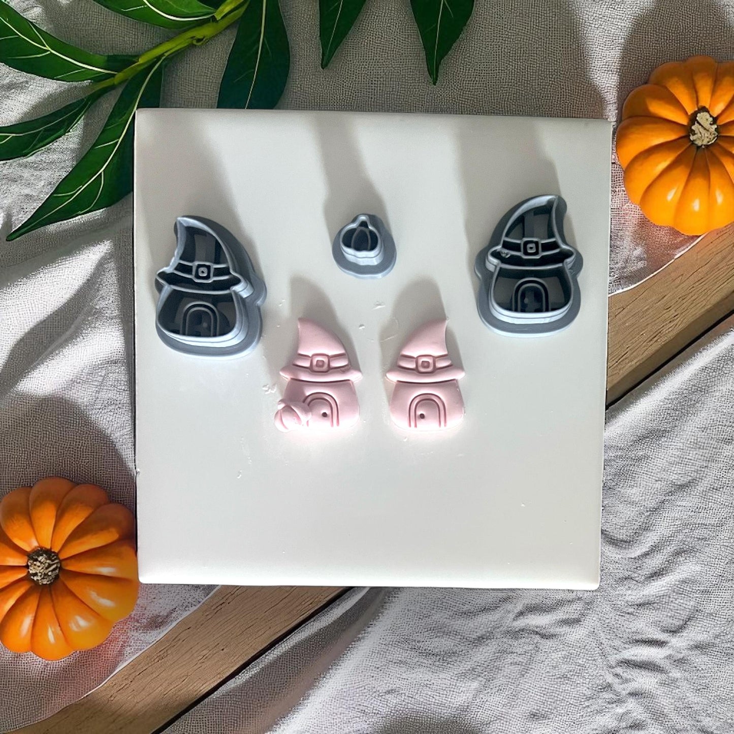 Witch hat house cutters and clay pieces on white tile with pumpkins