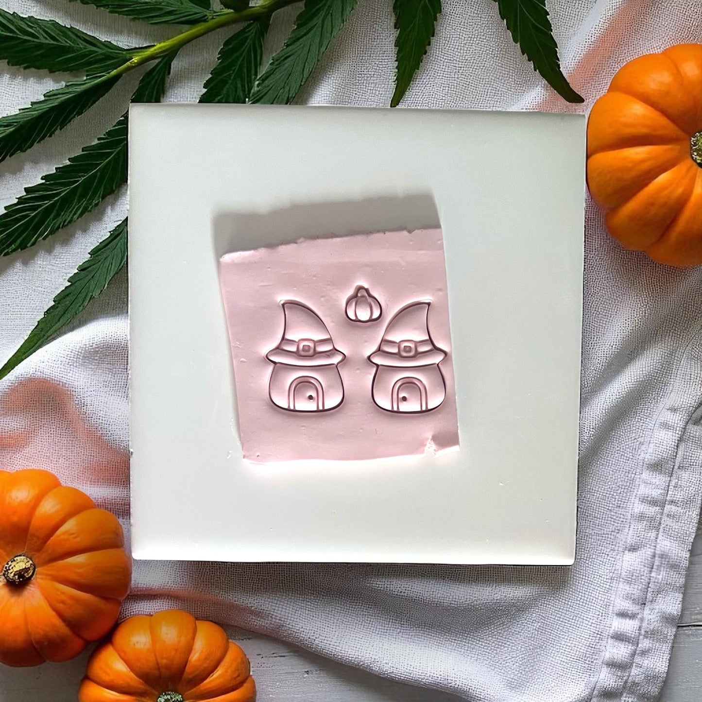 Pink clay imprints of witch hat houses and pumpkin on white tile