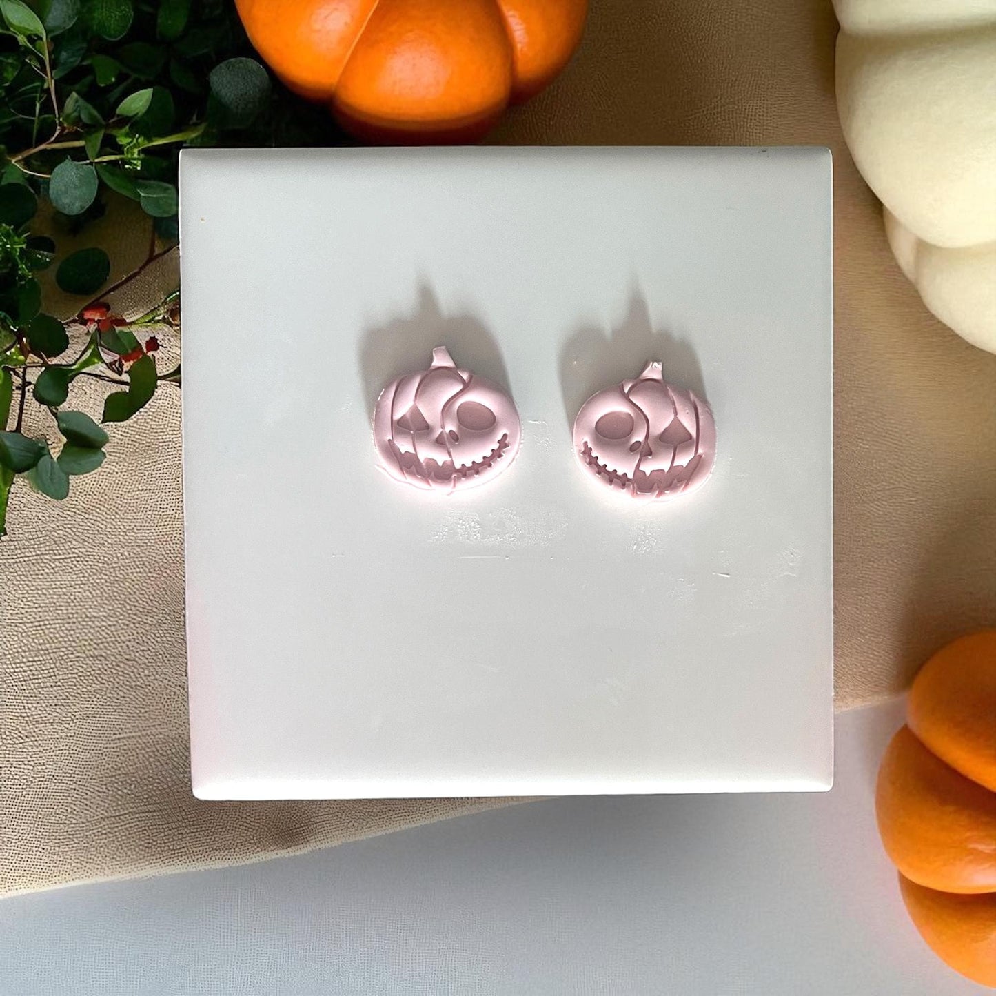 Two pink skull pumpkin clay pieces on tile with pumpkins