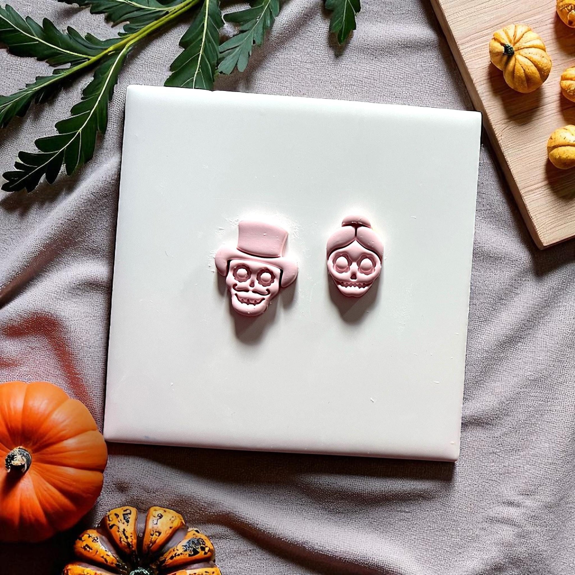 Finished clay skull couple in hat and bun on white tile with pumpkins