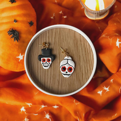 Finished clay earrings of bride and groom skulls with red eyes on orange fabric