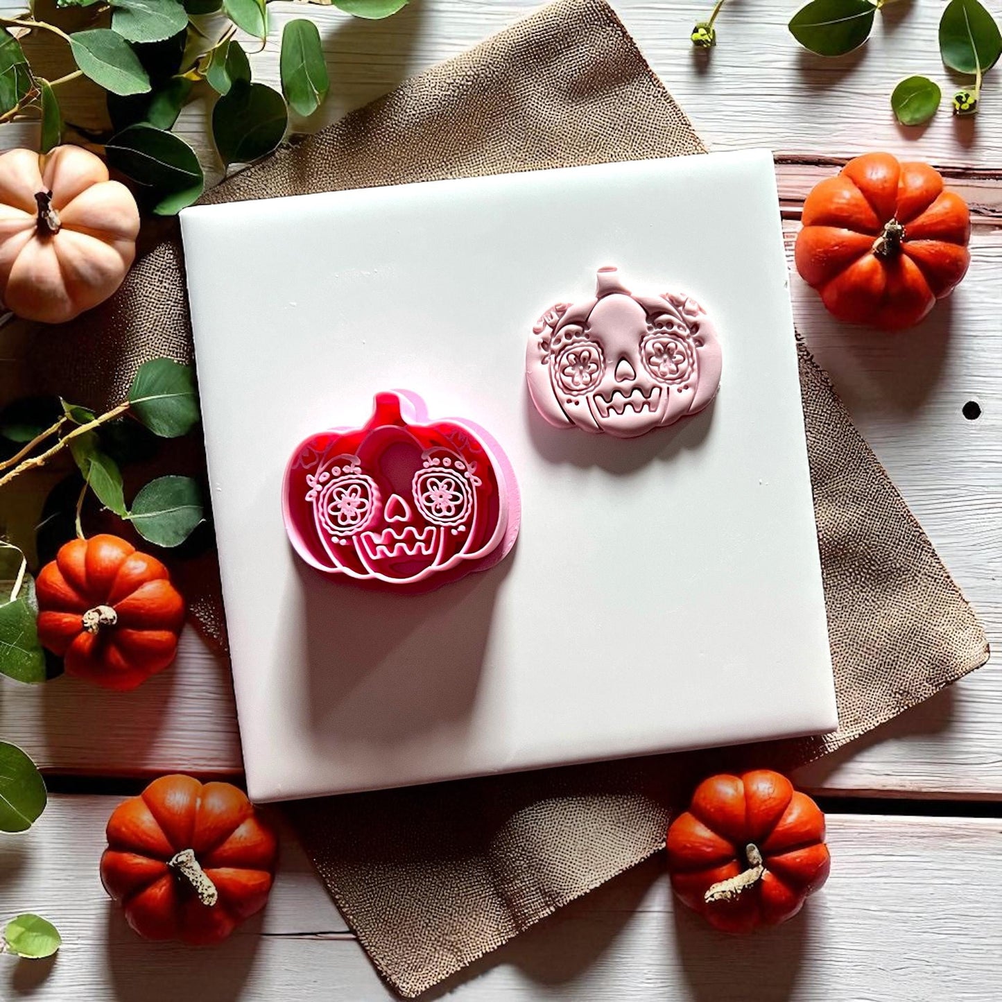 Pumpkin sugar skull clay cutter with imprint side by side on tile with pumpkins
