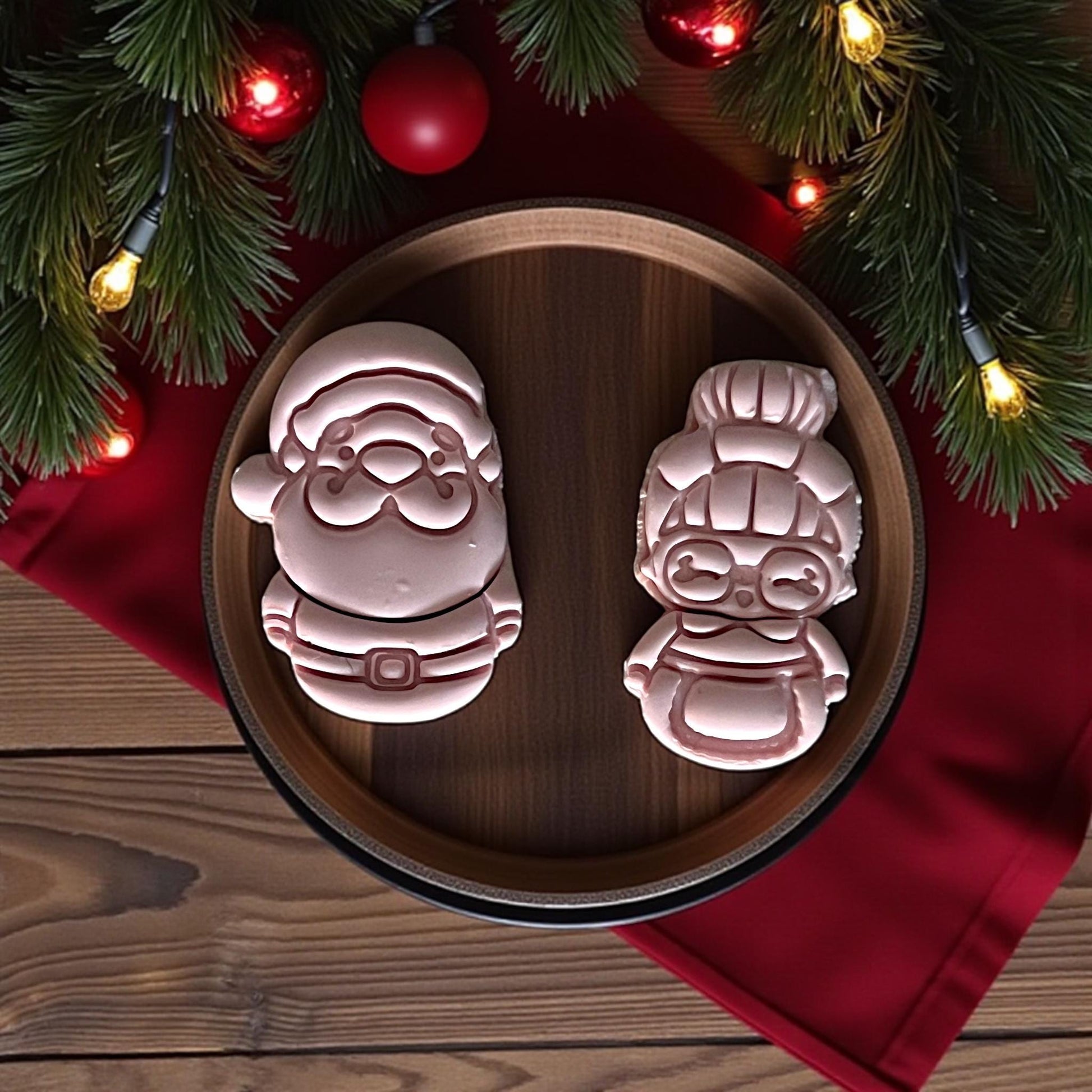 Pink clay Santa and Mrs Claus cutouts on wooden plate with red fabric and holiday greenery