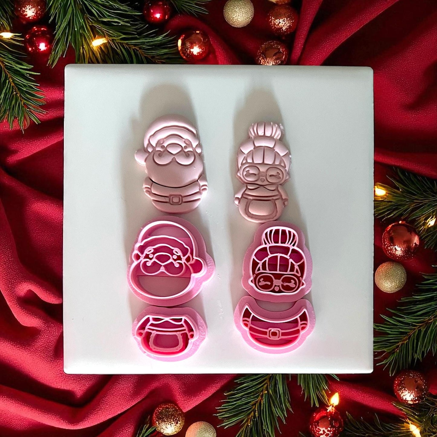 Santa and Mrs Claus clay cutters with pink clay impressions side by side on white tile